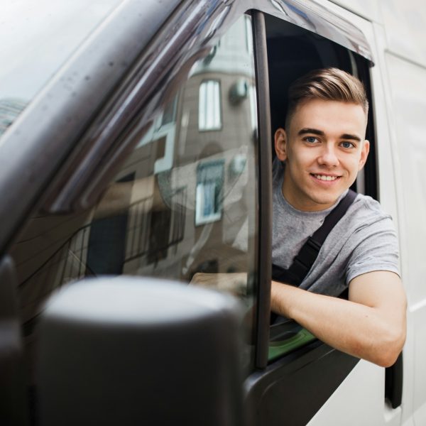 A young handsome smiling guy wearing uniform is looking out of the car window. House move, mover